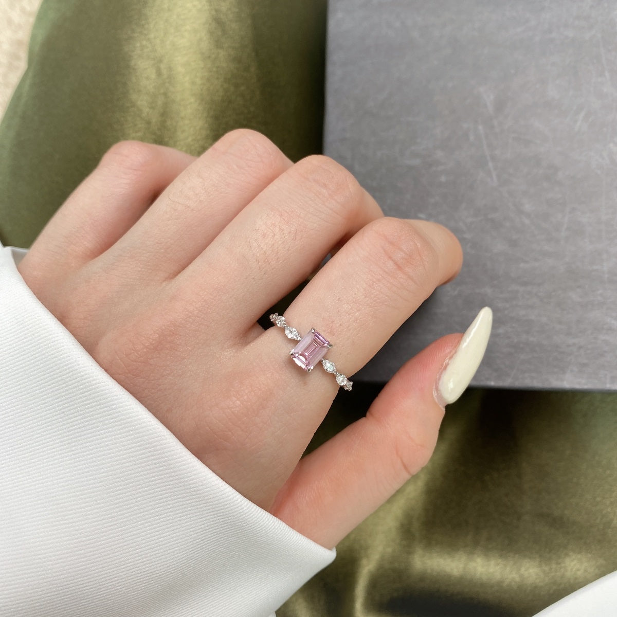 Hand wearing a ring with a pink gemstone on a green fabric background