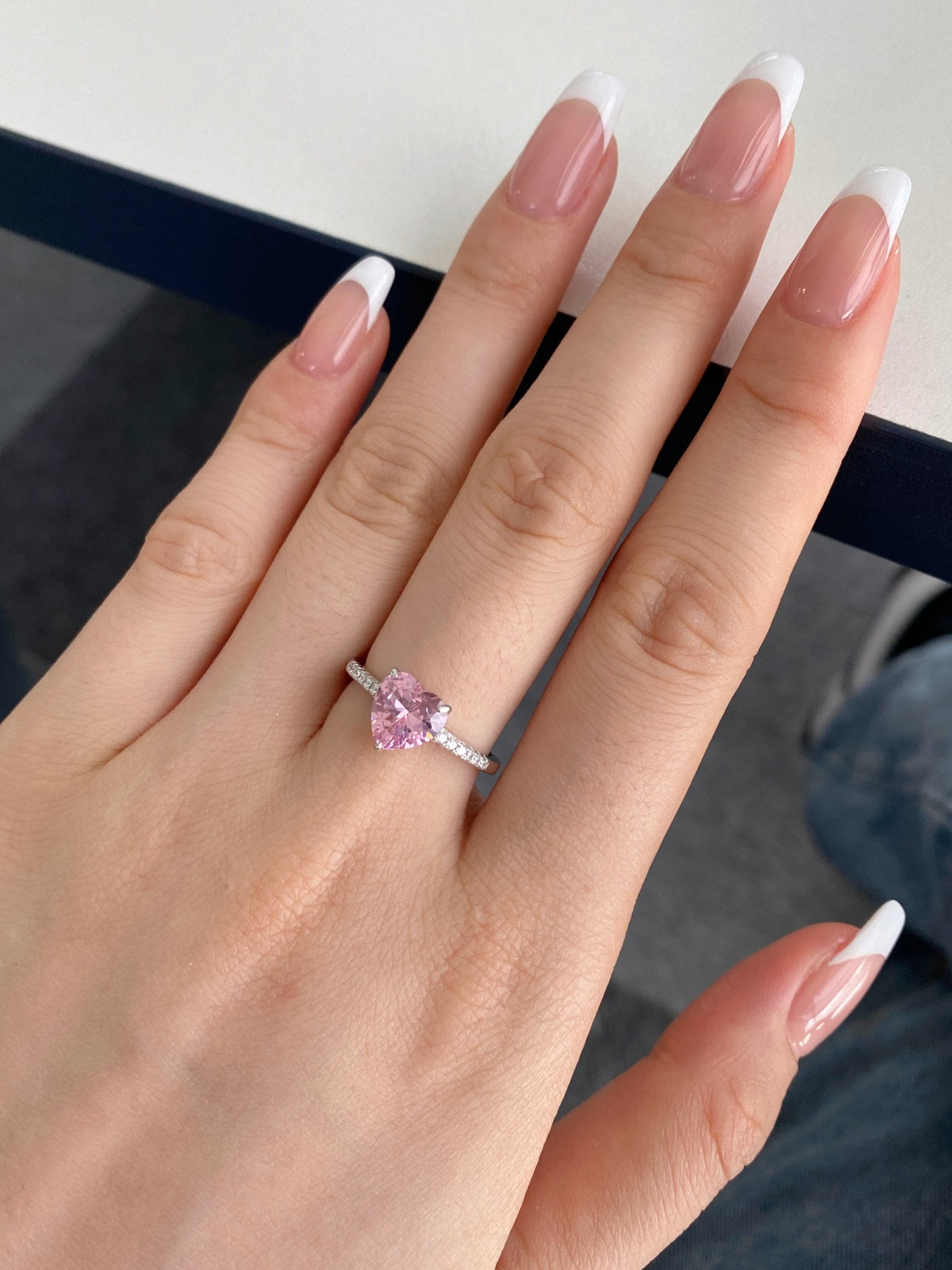 Hand wearing a ring with a pink gemstone on a neutral background