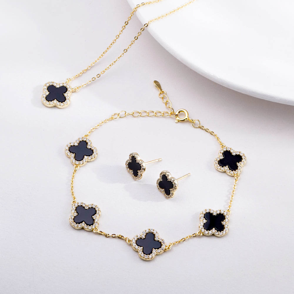 Gold jewelry set with black clover-shaped stones on a white background