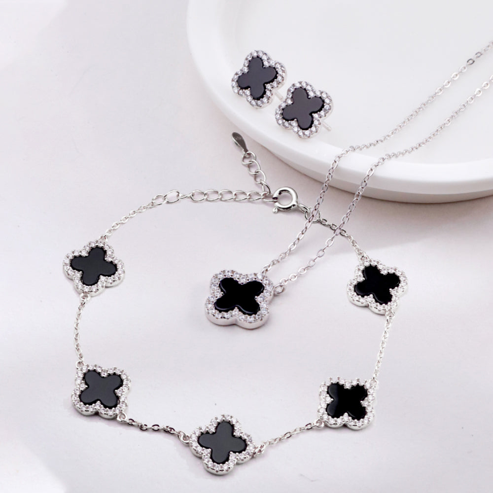 Jewelry set with necklace, bracelet, and earrings featuring black clover-shaped stones on a white background.