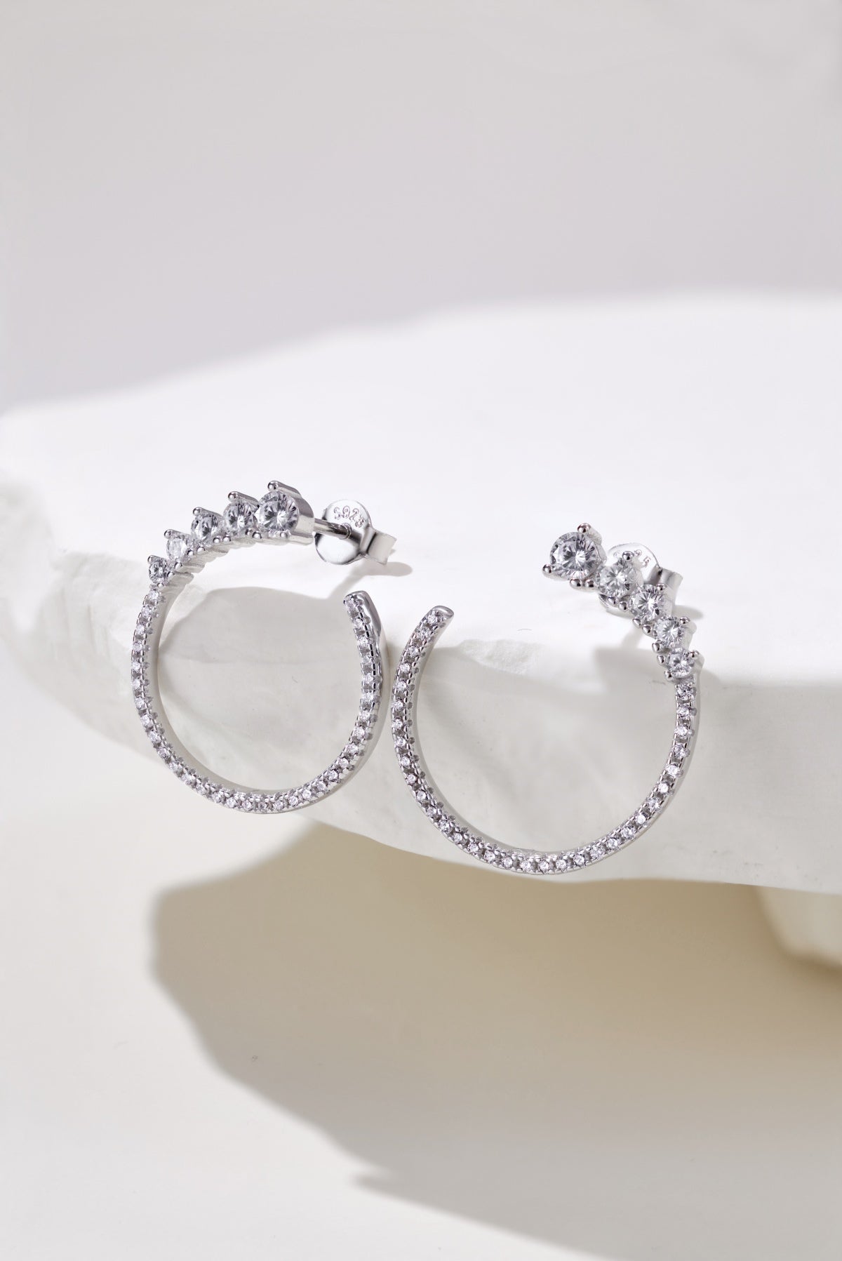 Silver hoop earrings with clear gemstones on a white background