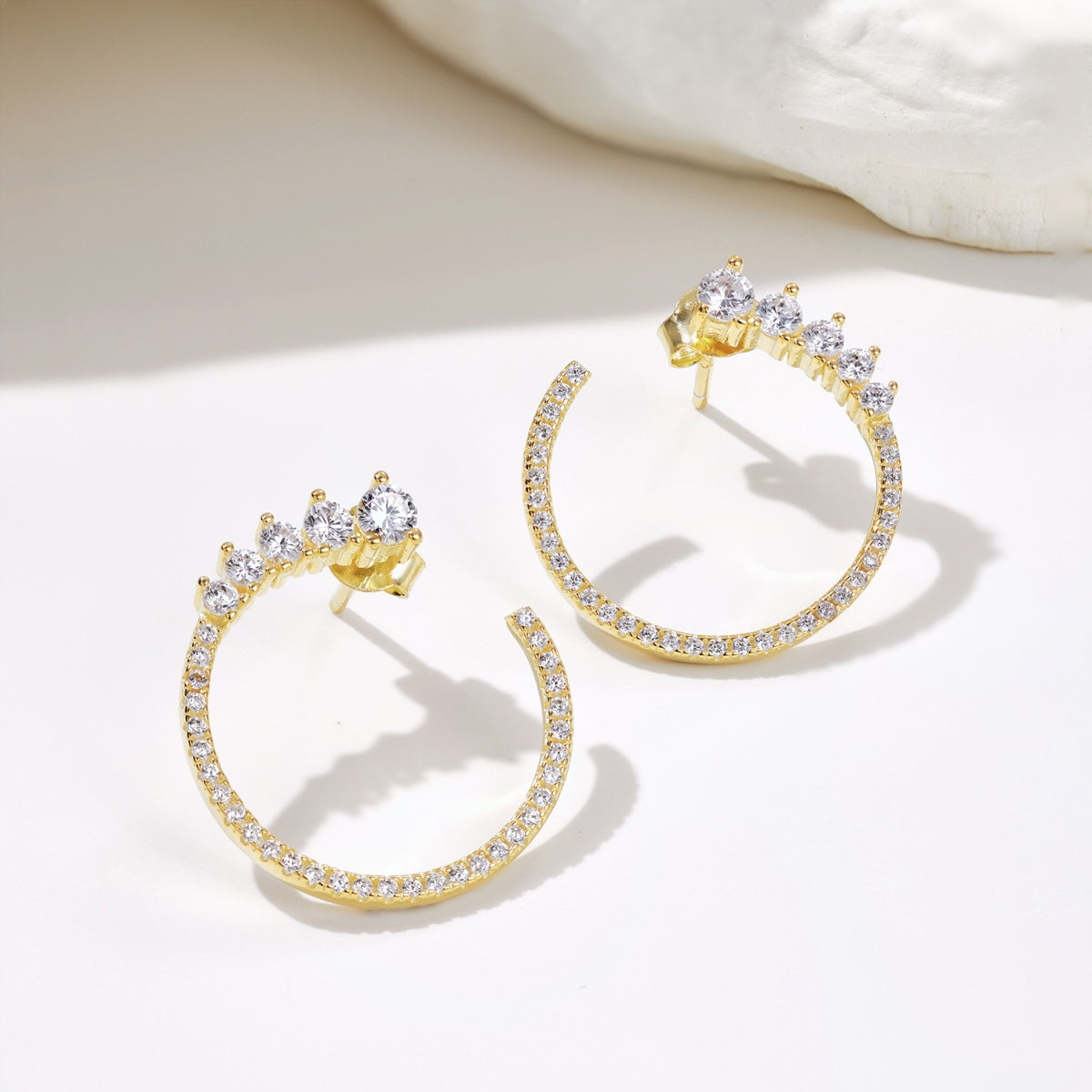 Gold hoop earrings with clear gemstones on a light background