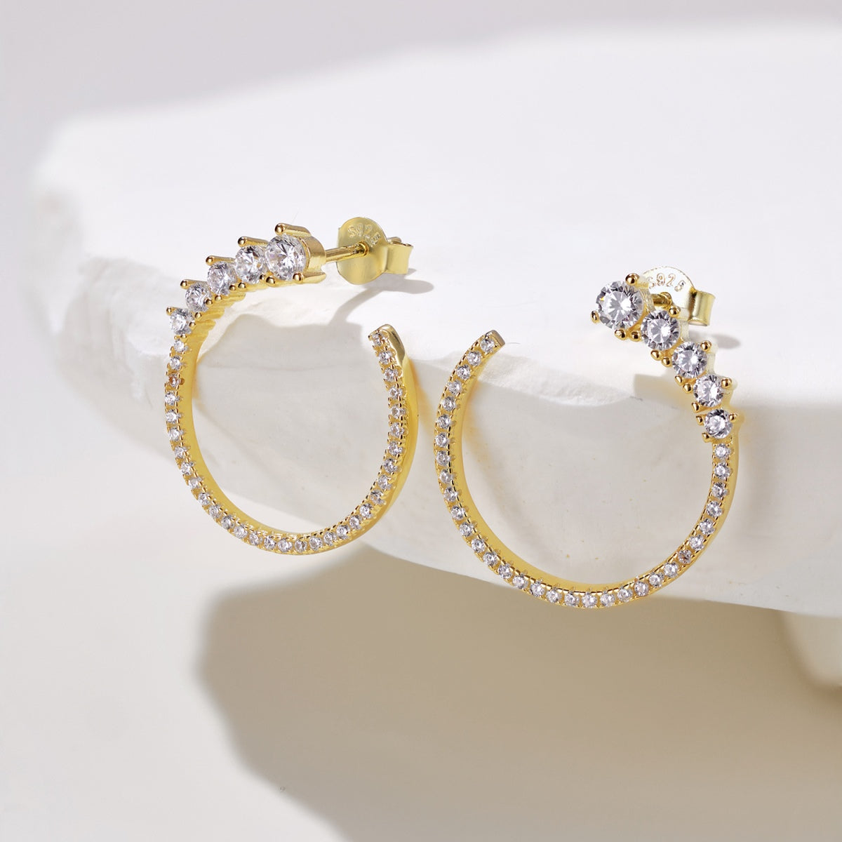 Gold hoop earrings with clear gemstones on a white surface