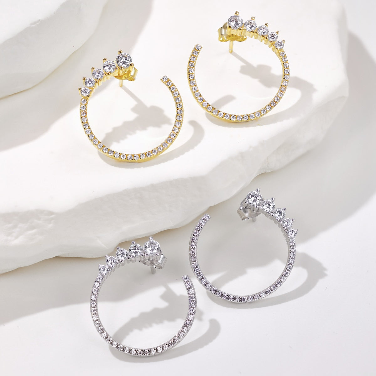 Pair of gold hoop earrings with clear gemstones on a white surface