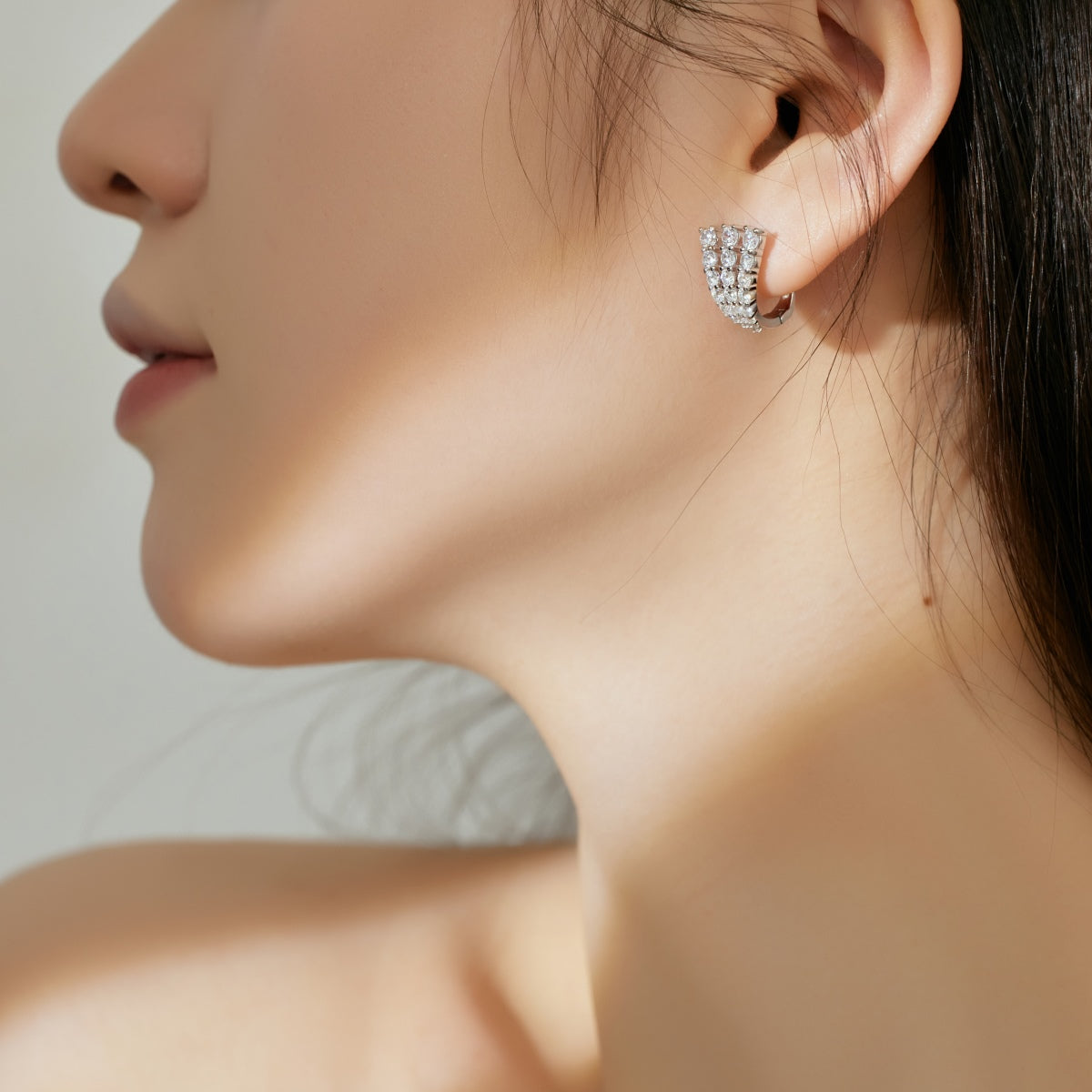 Close-up of a woman wearing a silver hoop earring against a neutral background