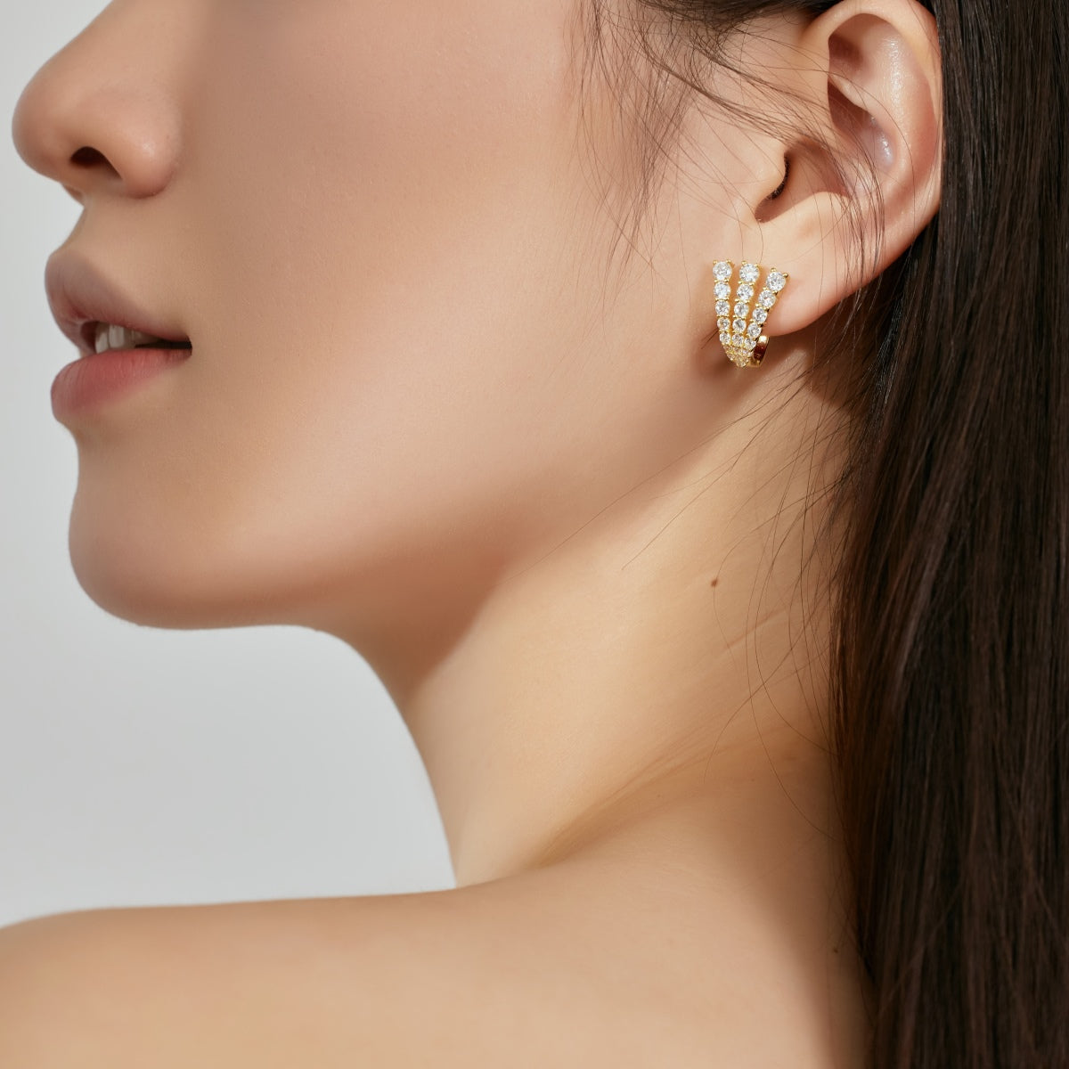 Close-up of a woman wearing a gold earring with small stones on a neutral background