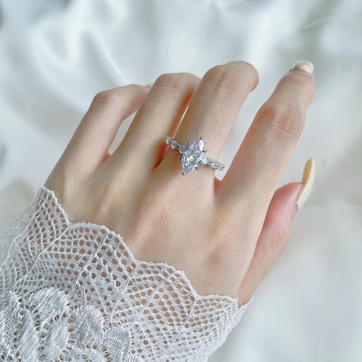 Hand wearing a silver marquise ring with a clear gemstone on a white background