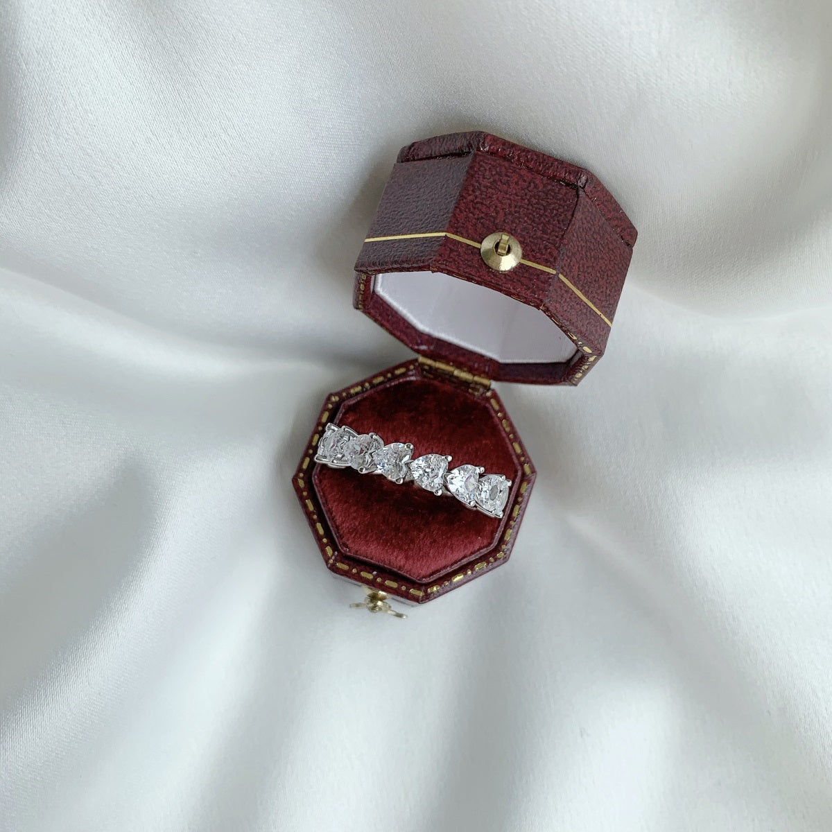 Open burgundy jewelry box with a diamond ring on a white fabric background