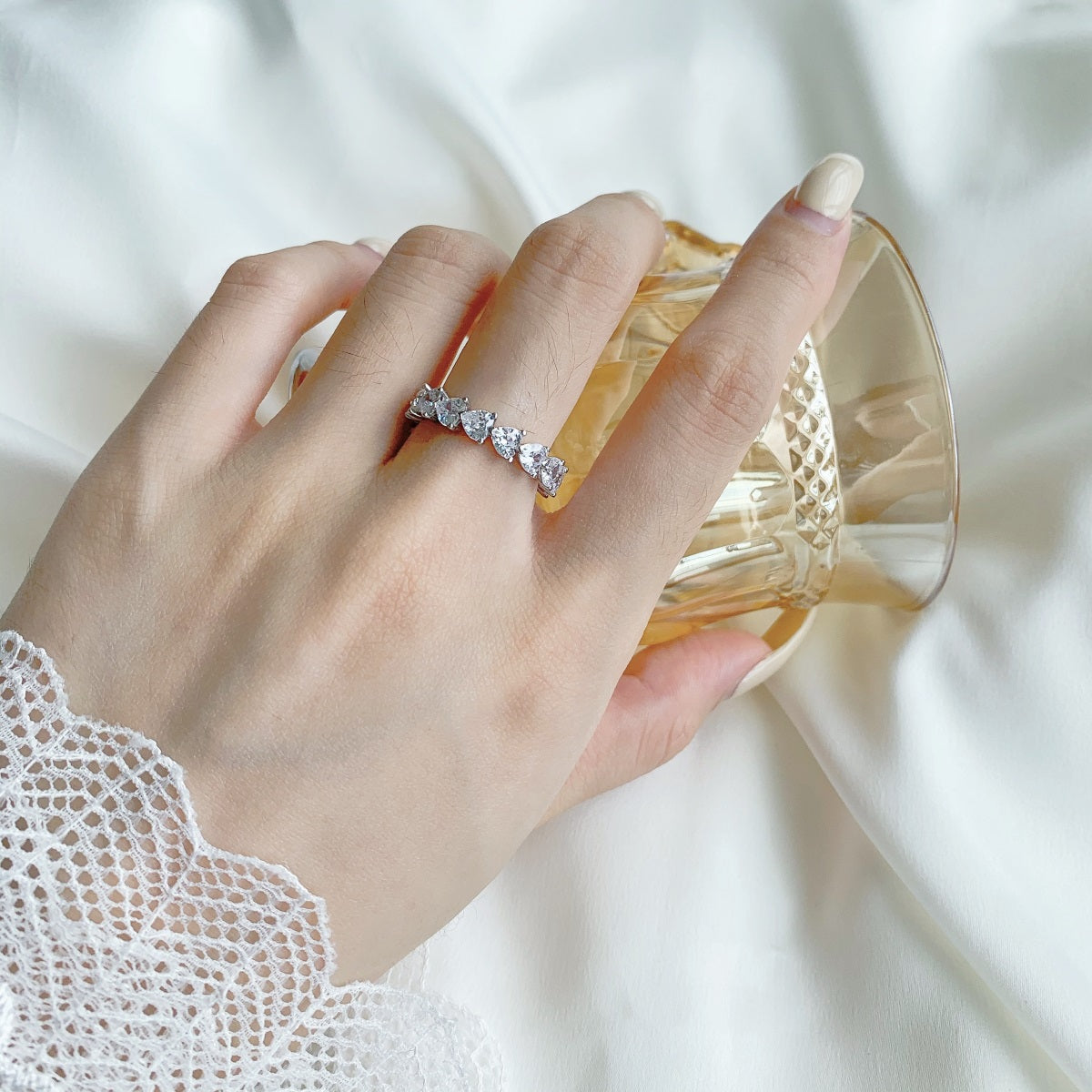 Hand wearing a diamond ring holding a glass with a white background