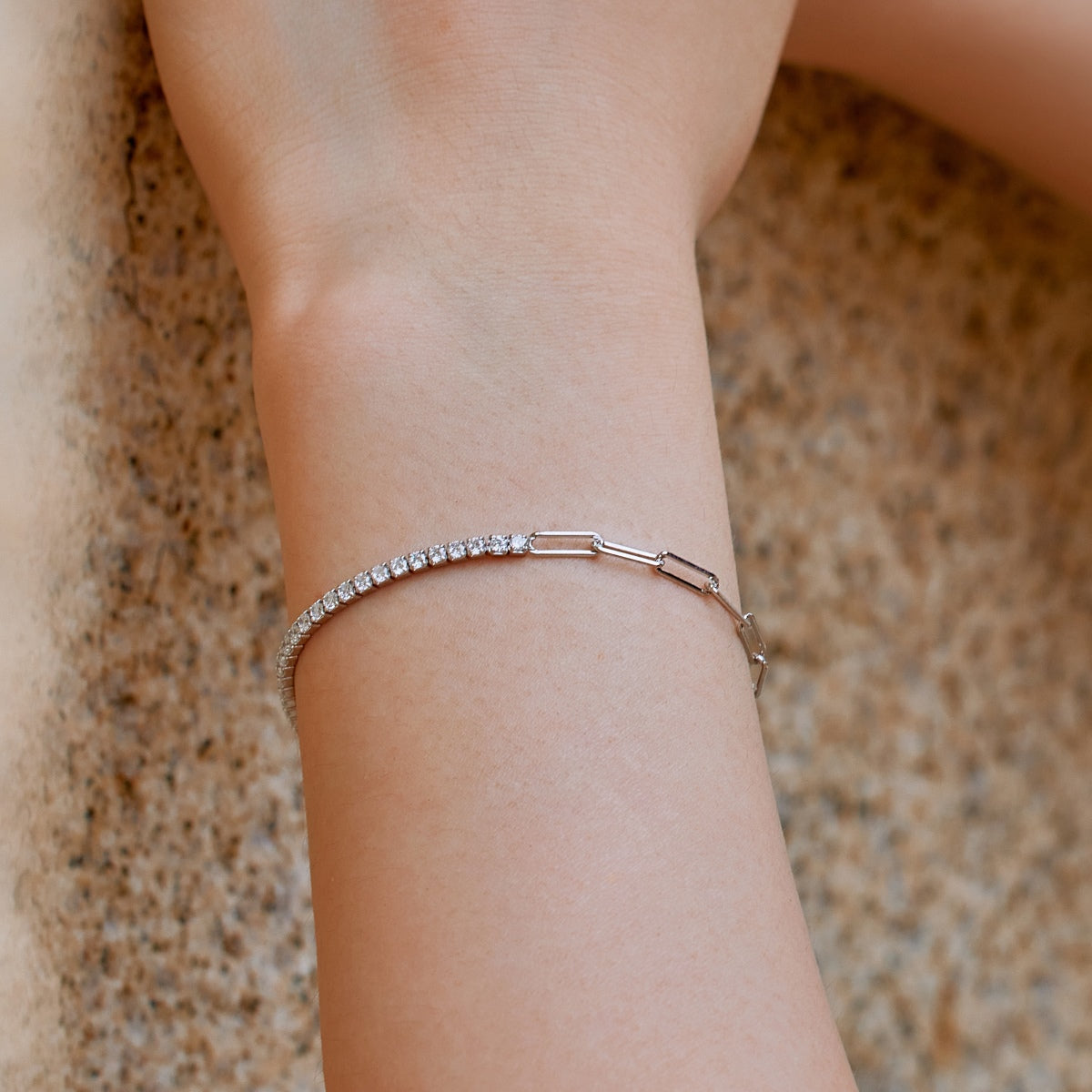 silver tennis paperclip bracelet with diamonds on a wrist against a neutral background