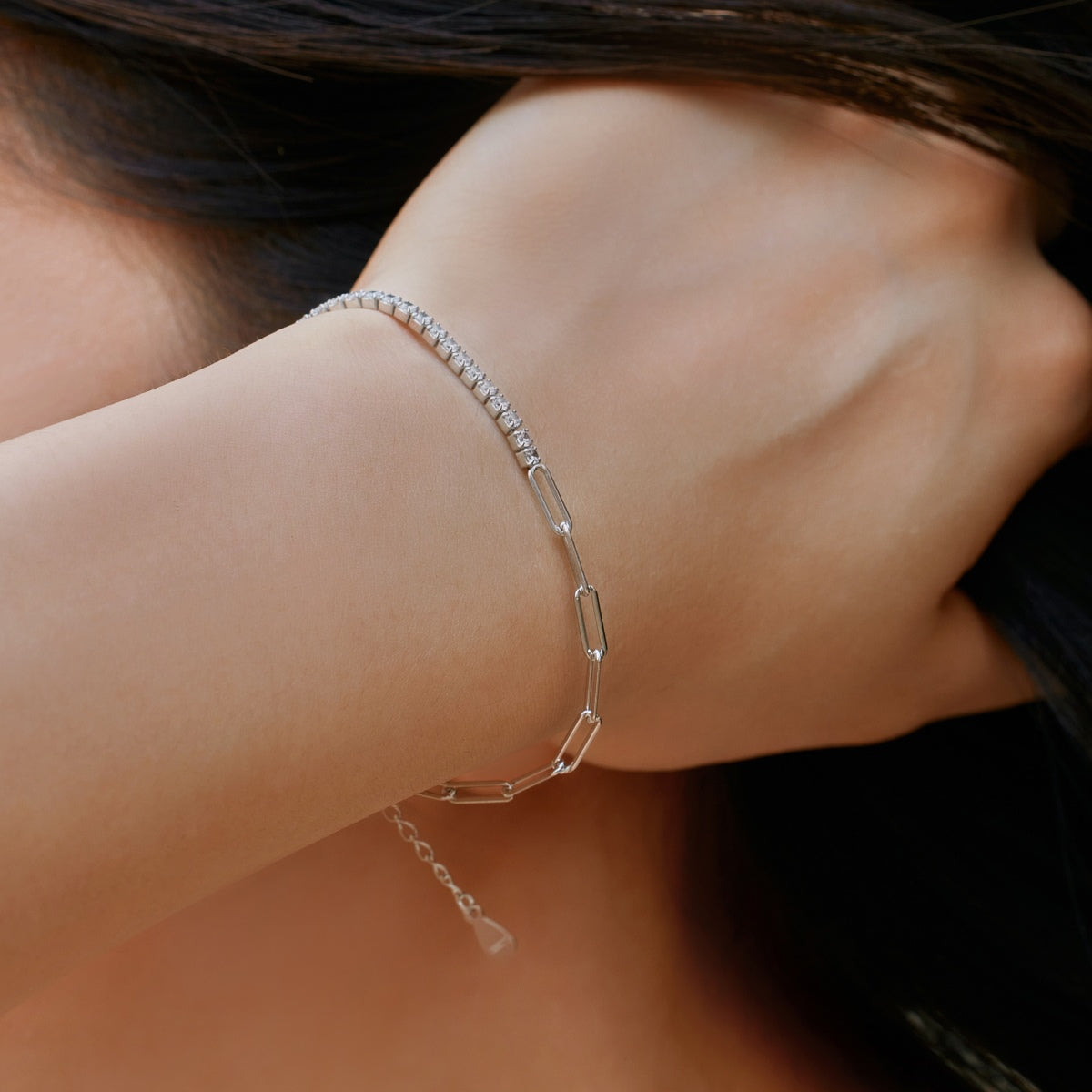 Close-up of a person wearing a silver tennis paperclip bracelet on their wrist.