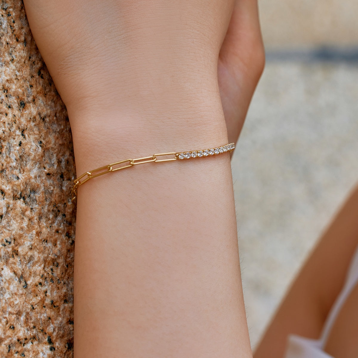 Gold paperclip chain tennis bracelet on a wrist with a blurred background