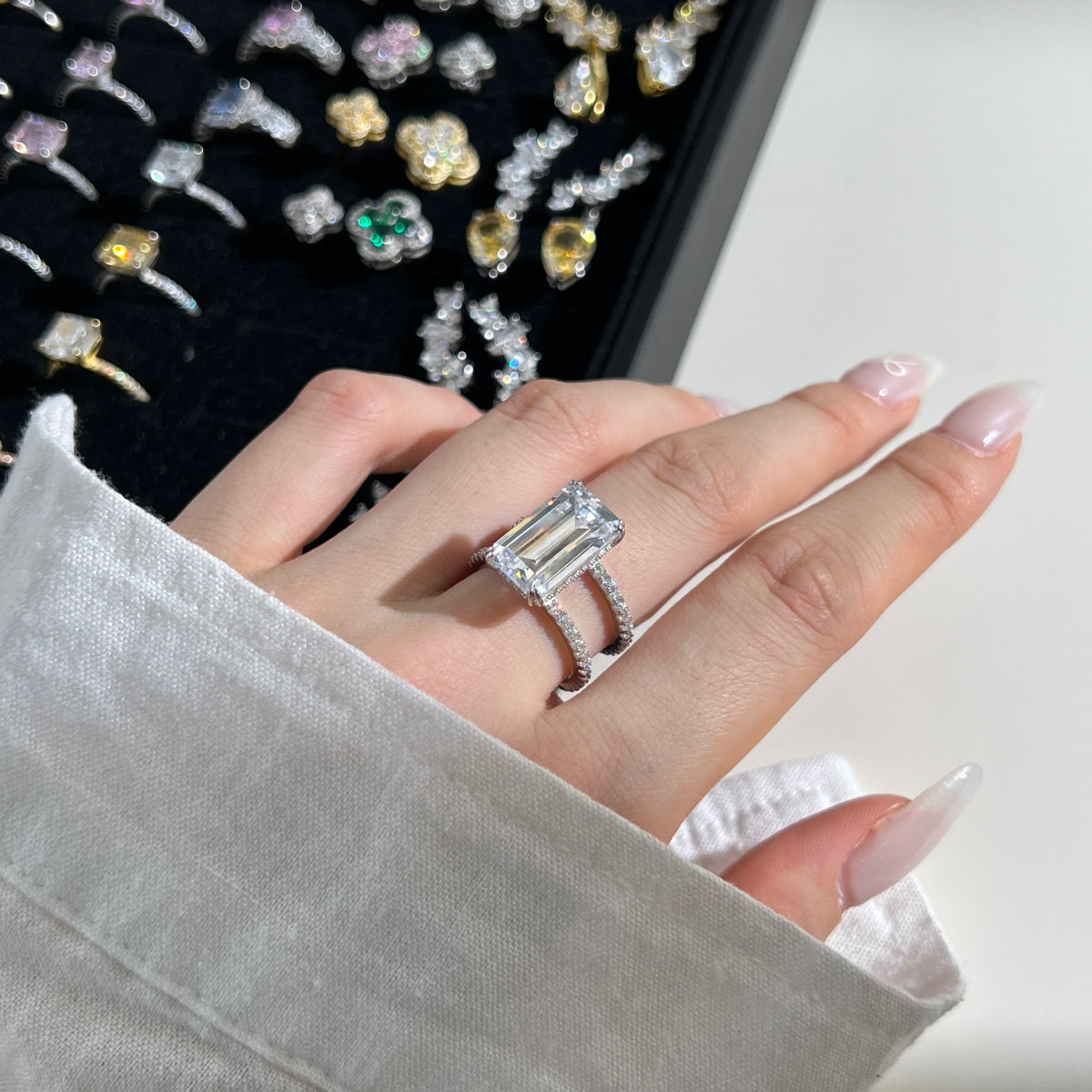 Hand wearing a diamond ring with a blurred background of more jewelry.