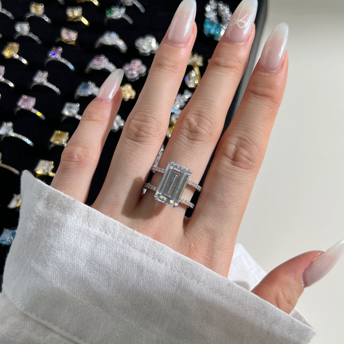 Hand wearing a silver ring with a diamond, set against a background of other rings.