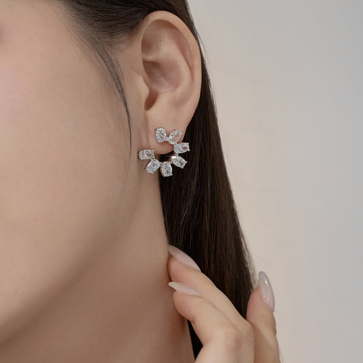 Close-up of a person wearing a silver zircon stud earring with a blurred background