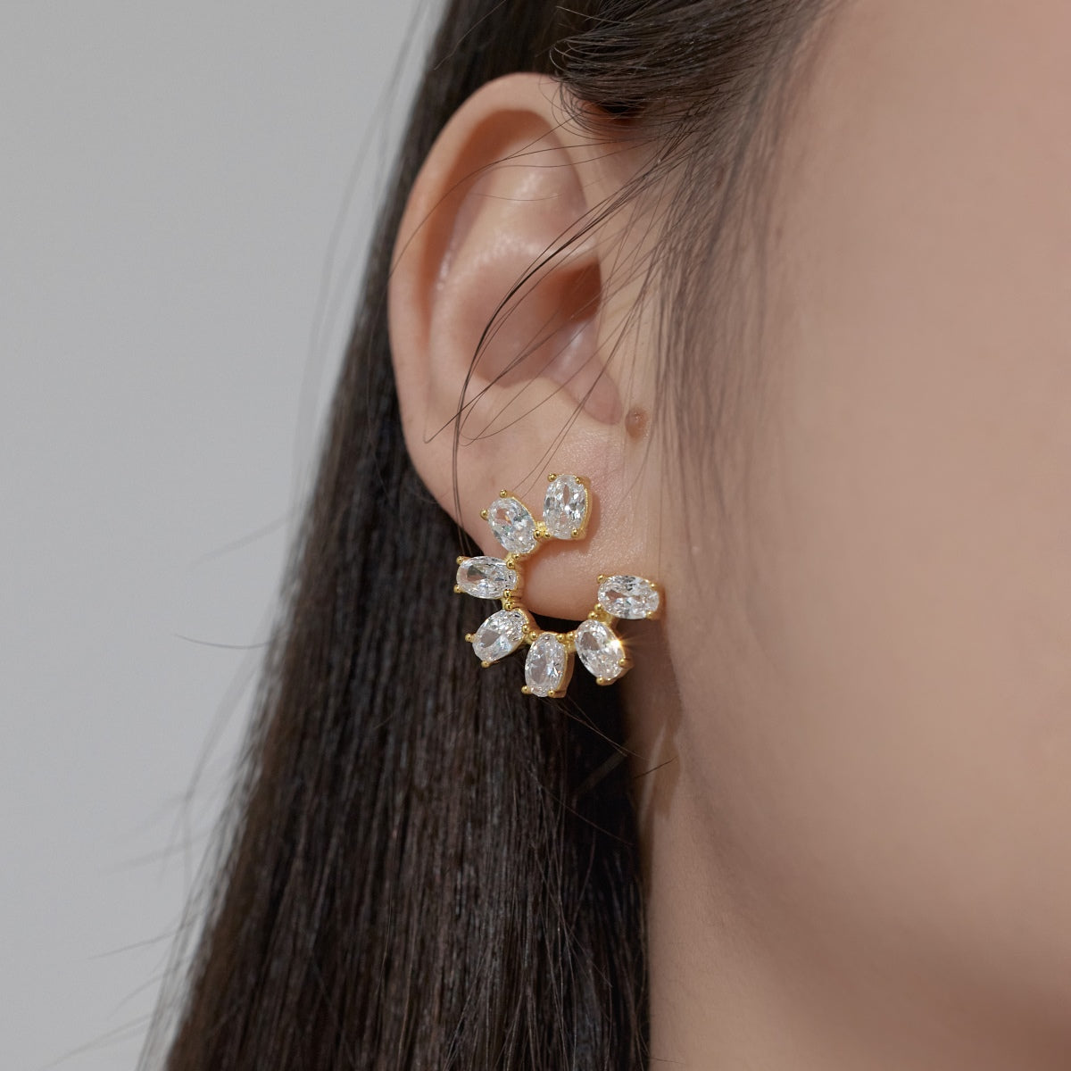 Close-up of an ear wearing a gold earring with clear stones on a neutral background