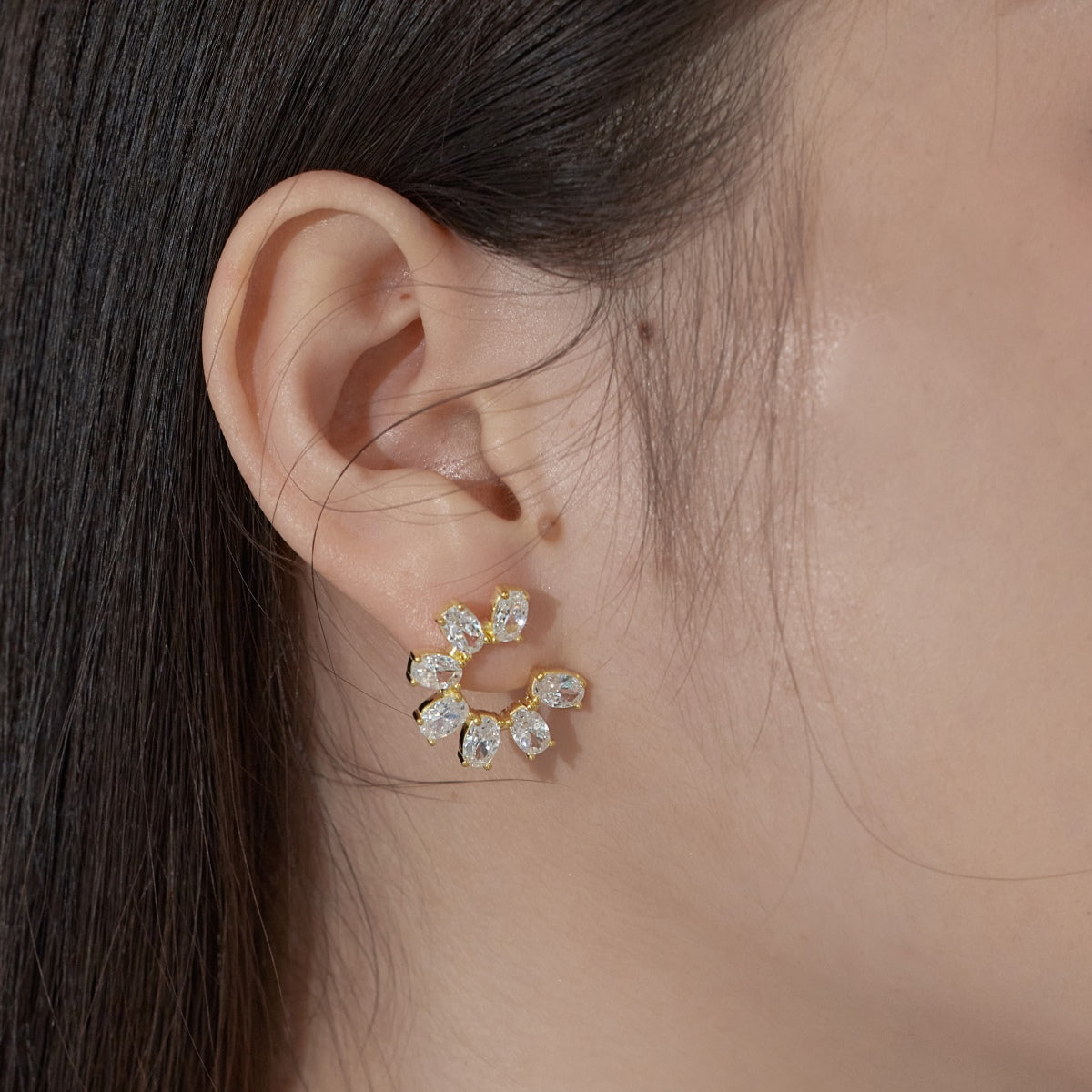 Close-up of an ear wearing a gold and diamond earring with a blurred background