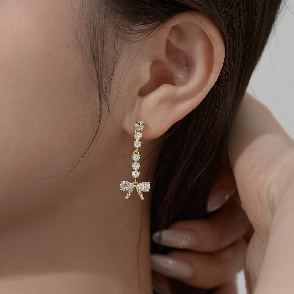Close-up of an ear wearing a diamond earring with a bow design.