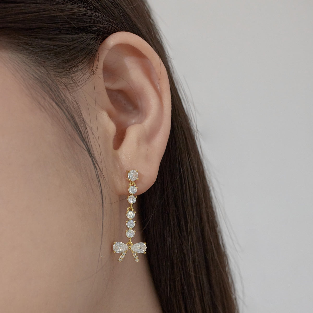Close-up of an ear wearing a gold and diamond earring against a neutral background
