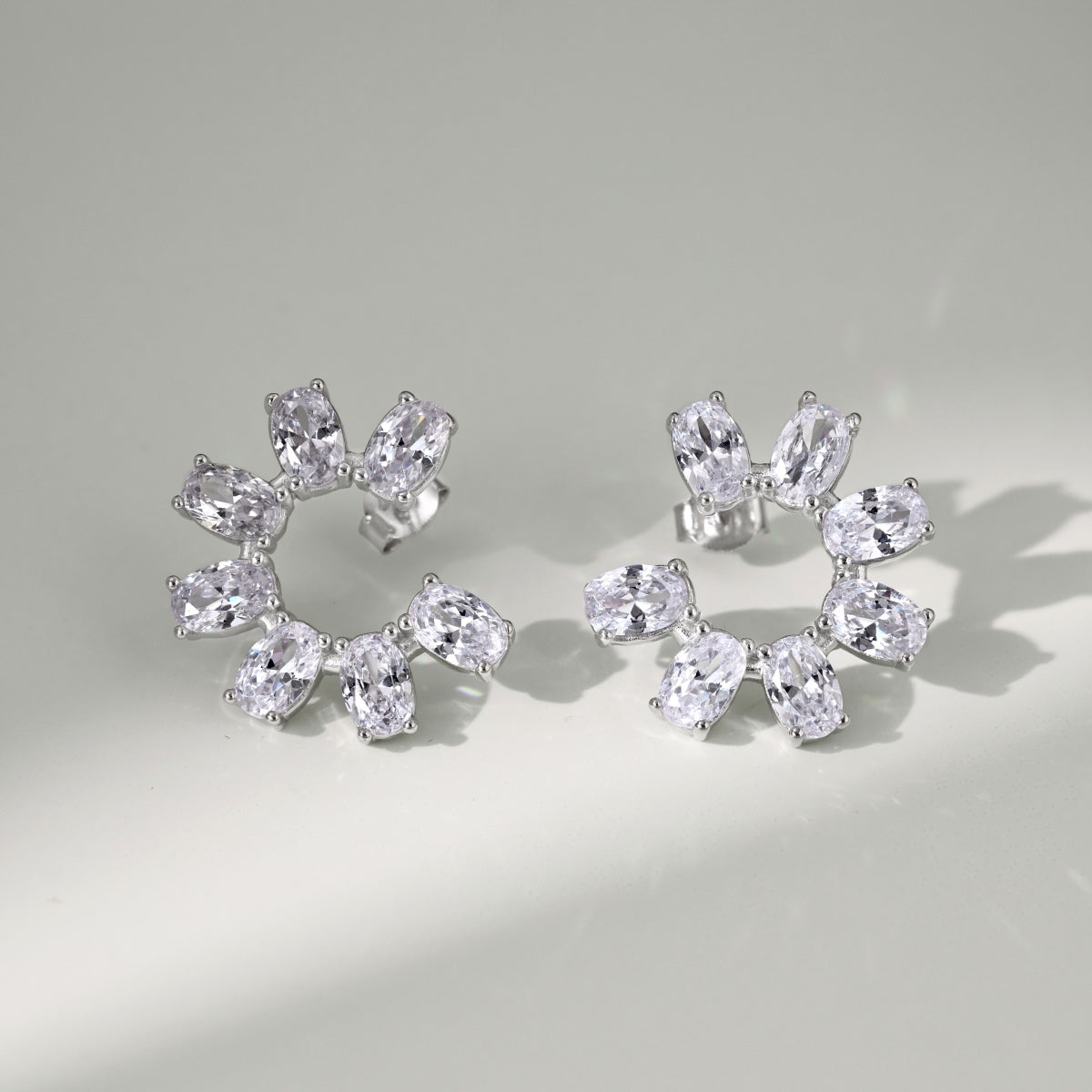Pair of silver hoop earrings with clear gemstones on a light gray background