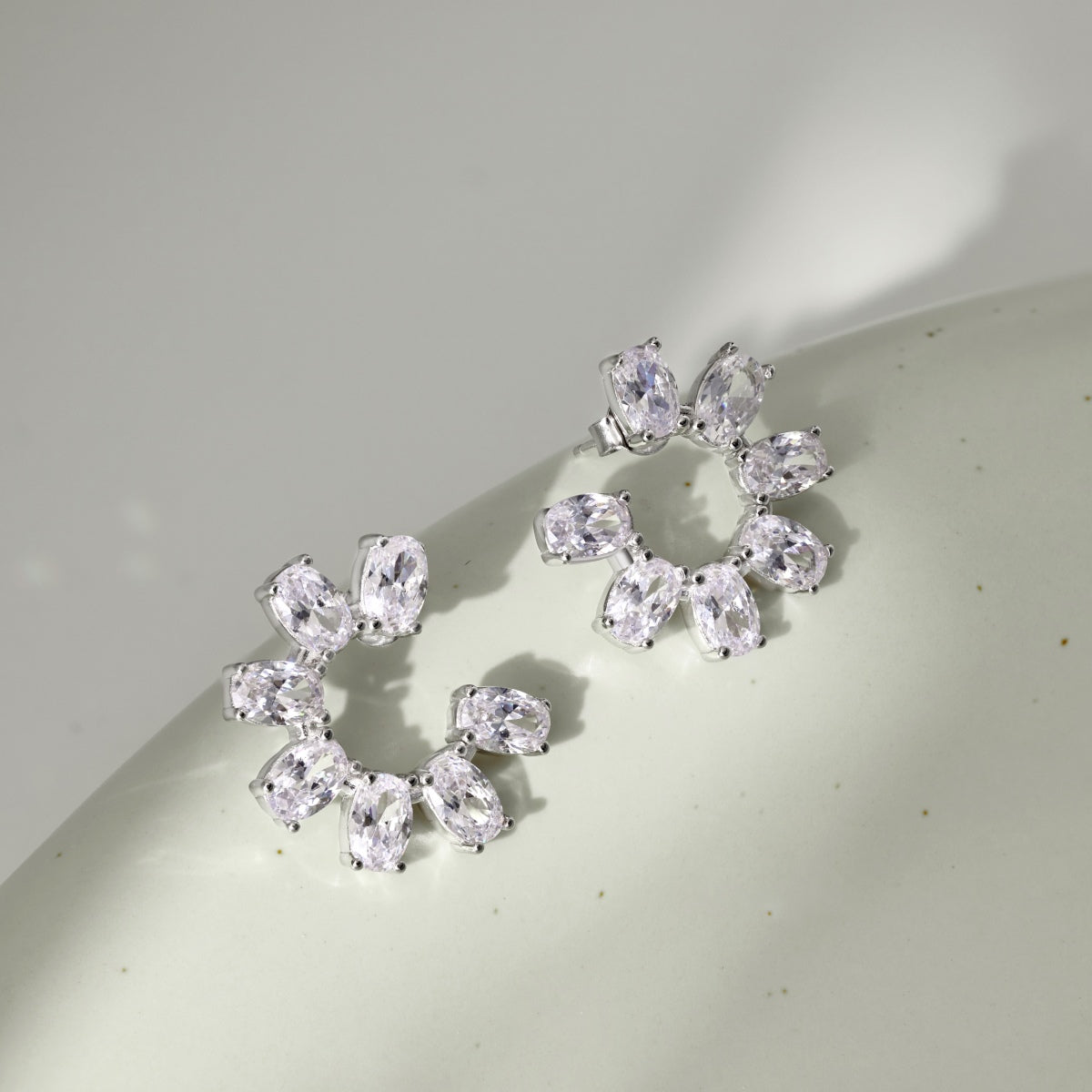 Pair of silver earrings with clear gemstones on a light gray background