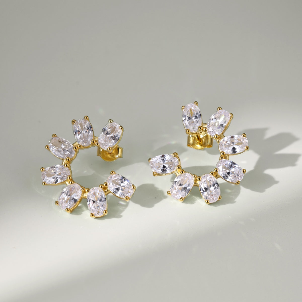 Gold earrings with clear gemstones on a light gray background