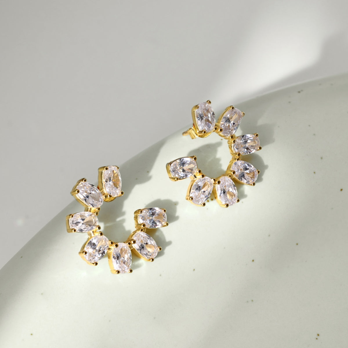 Gold hoop earrings with clear gemstones on a light background