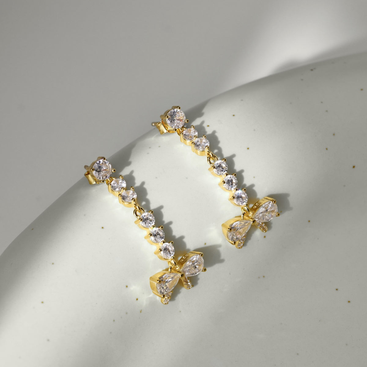 Gold earrings with clear gemstones on a light gray surface