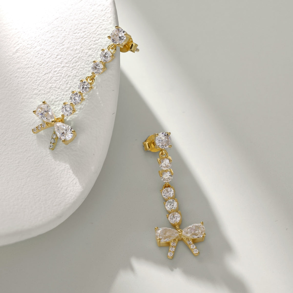 Gold bow-shaped earrings with clear gemstones on a white background