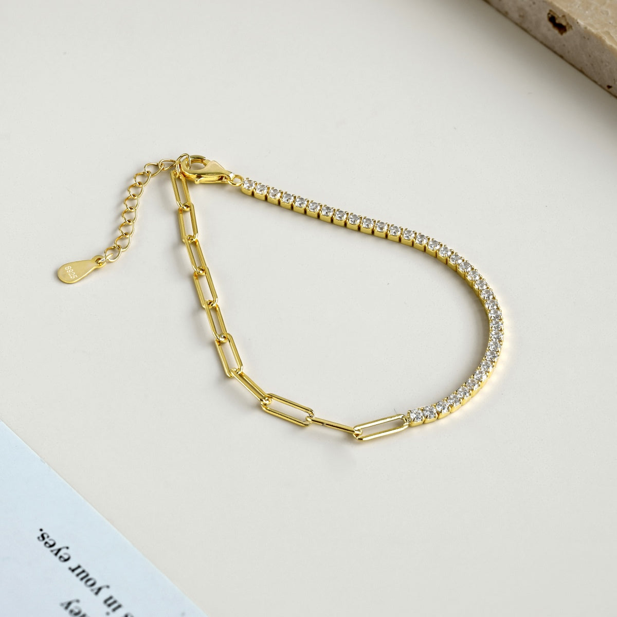 Gold paperclip chain tennis bracelet with clear stones on a light background
