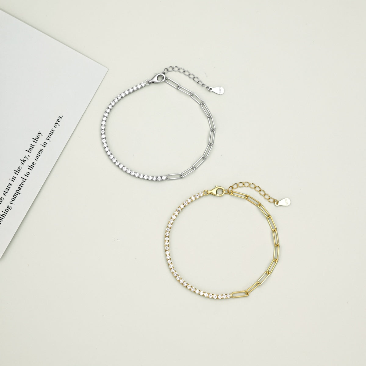 Two tennis paperclip chain bracelets, one silver and one gold, on a light gray background.