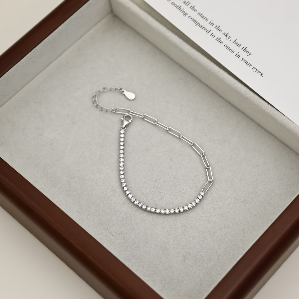 Silver tennis paperclip chain bracelet in a box with a quote on a light background