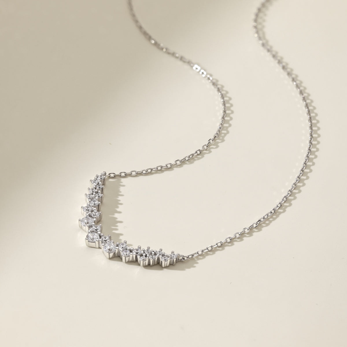 Silver necklace with diamond-like stones on curved pendant on a beige background