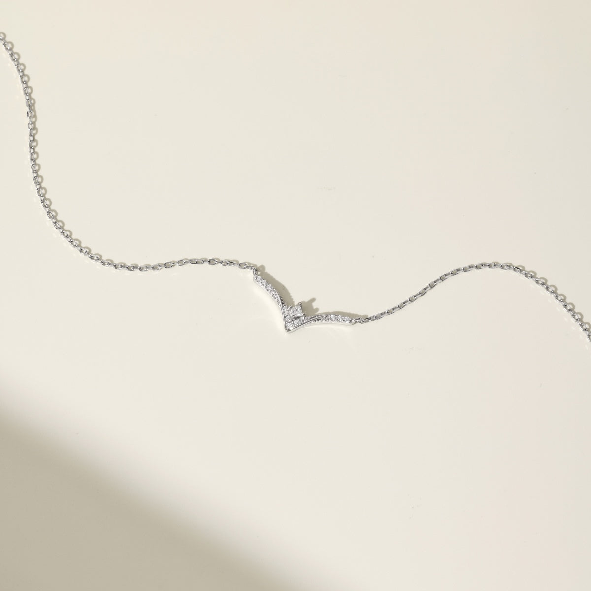 Silver necklace with a chevron pendant on a light beige background
