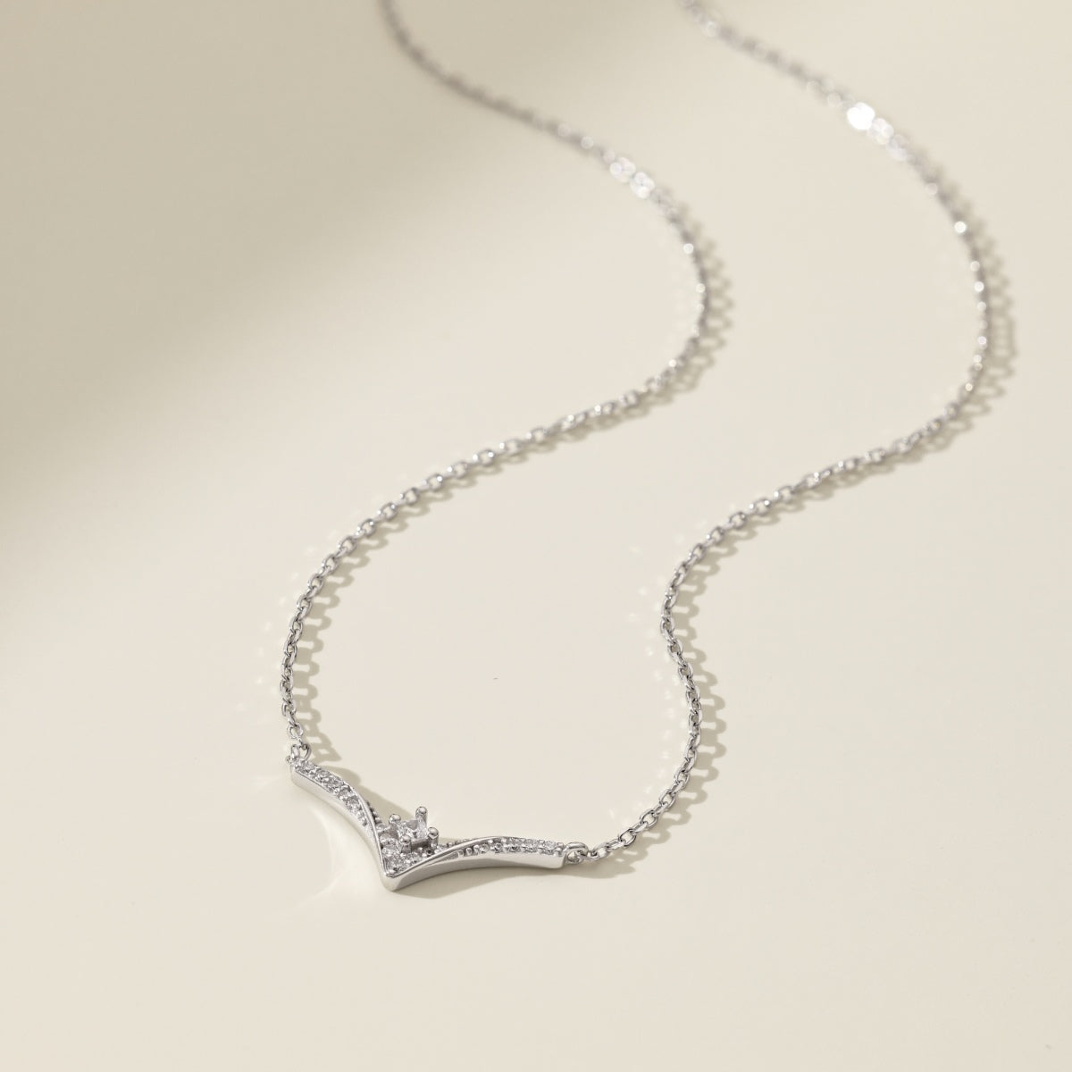 Silver necklace with a delicate chevron pendant on a light beige background
