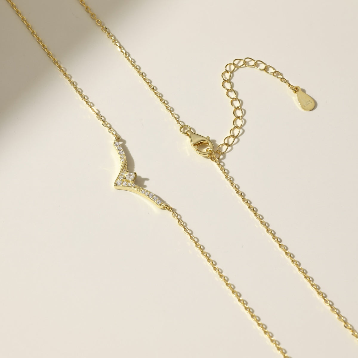 Gold necklace with a small chevron pendant on a beige background