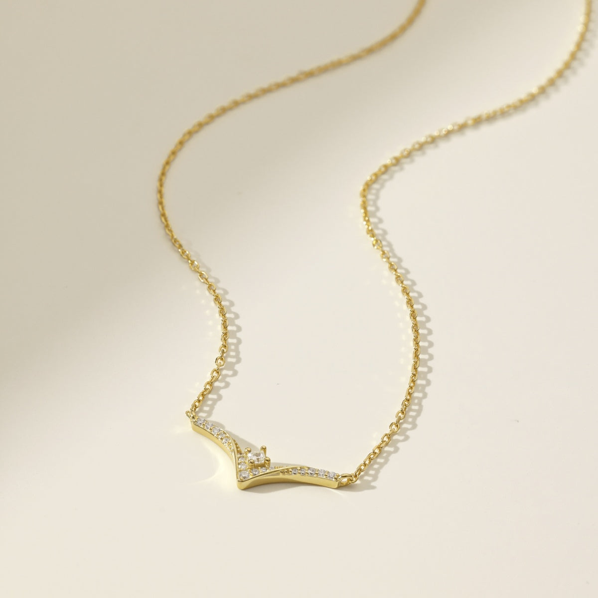 Gold necklace with a diamond chevron pendant on a beige background