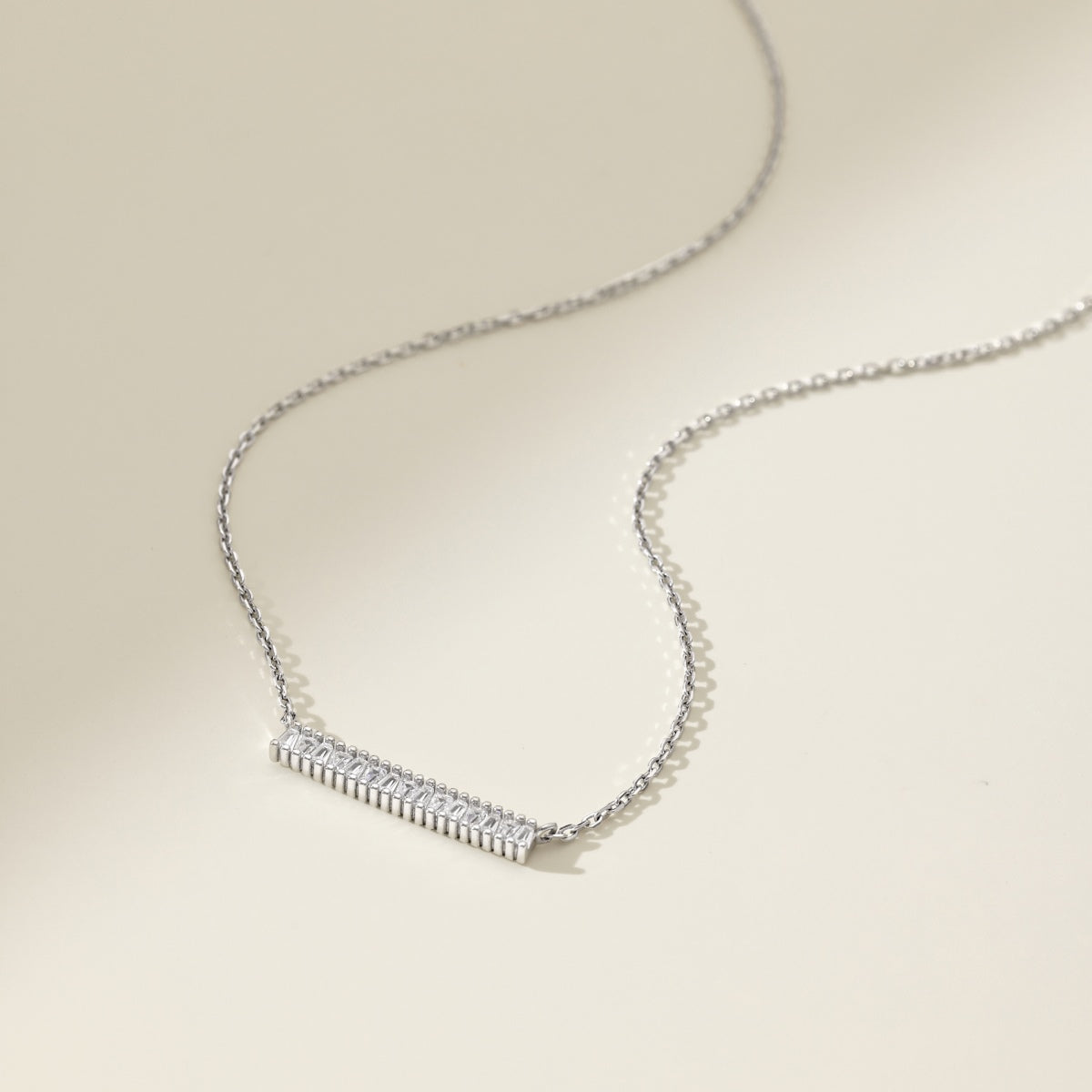 Silver necklace with a bar-shaped pendant on a beige background
