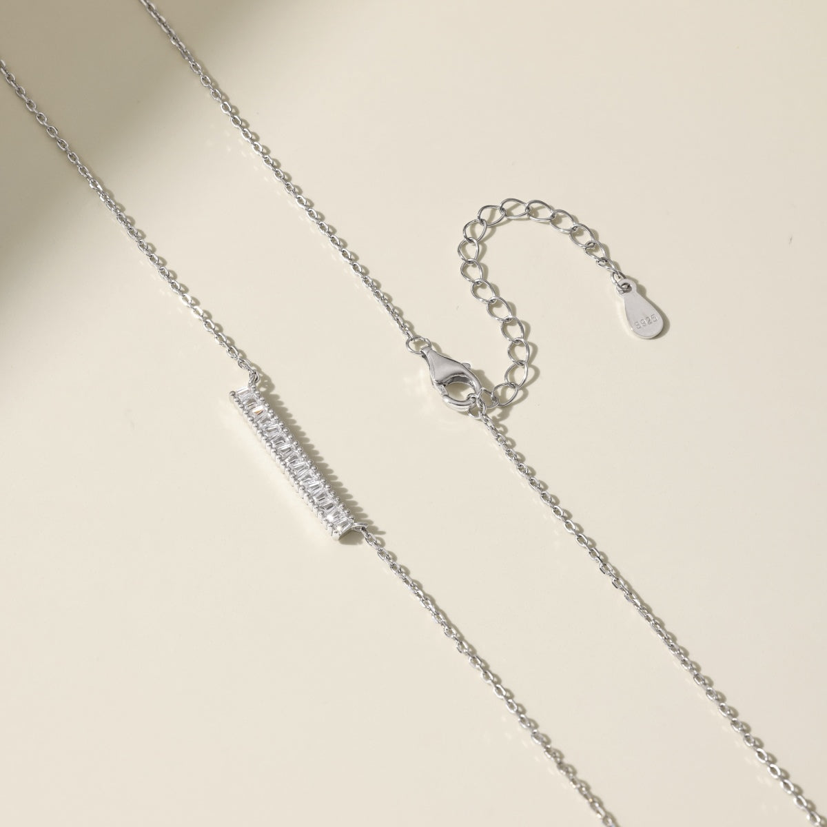 Silver necklace with a bar pendant on a beige background
