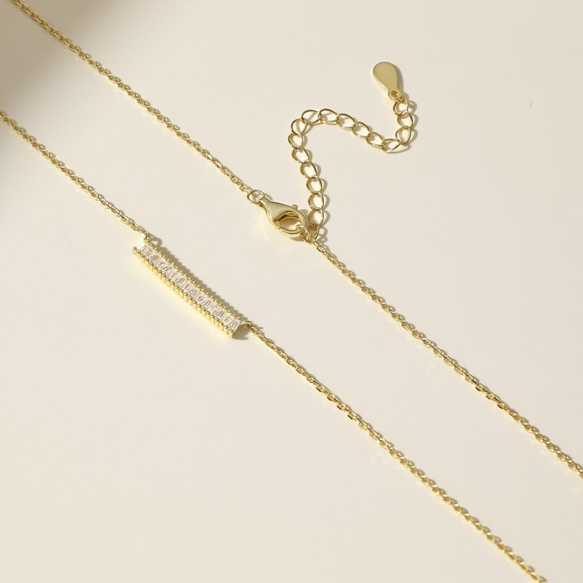 Gold necklace with a bar pendant on a beige background