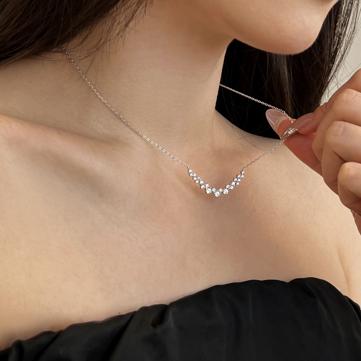 Person wearing a delicate silver diamond necklace with small stones.