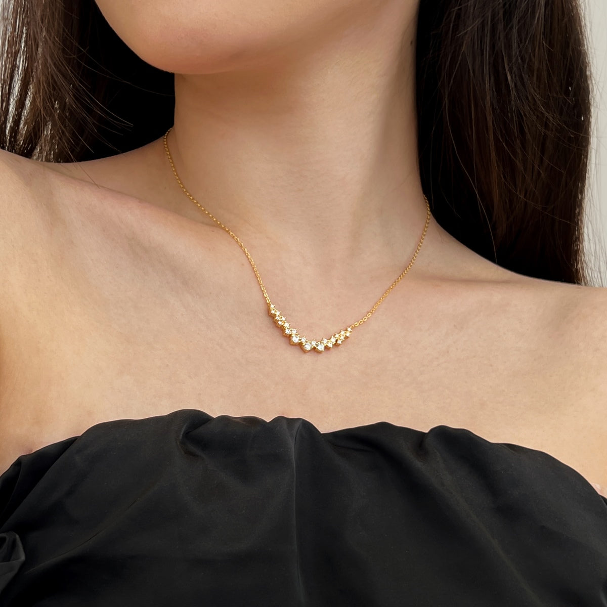 Gold curved pendant necklace worn by a person against a neutral background