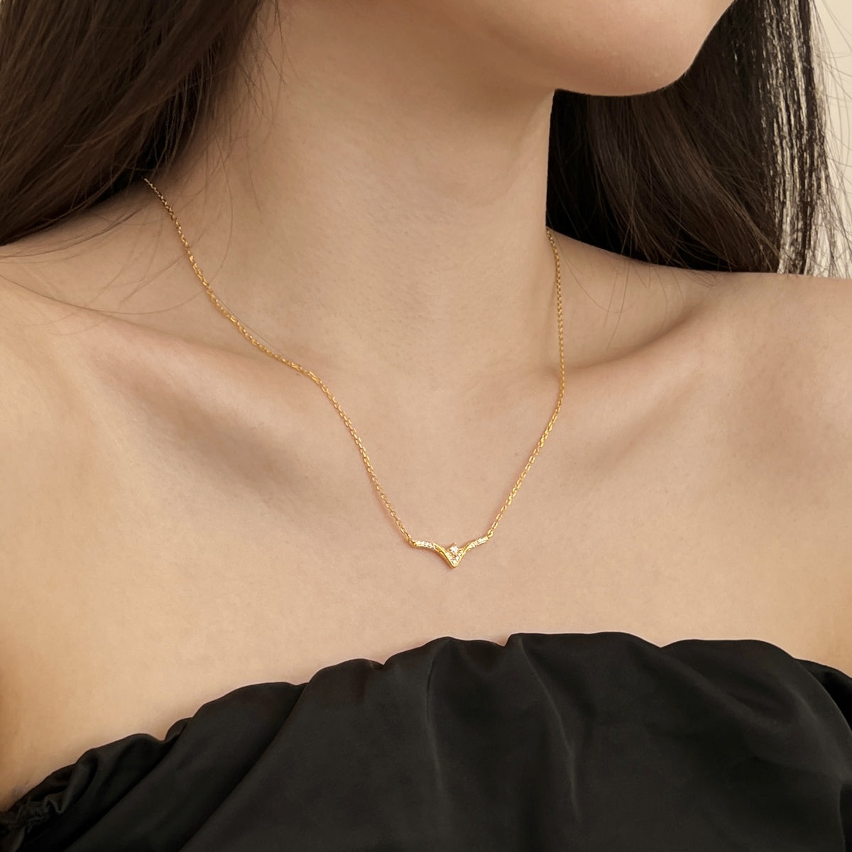 Gold necklace with a chevron pendant worn by a person