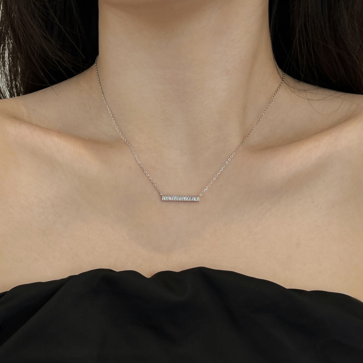 Necklace with a small pendant on a person wearing a black top.
