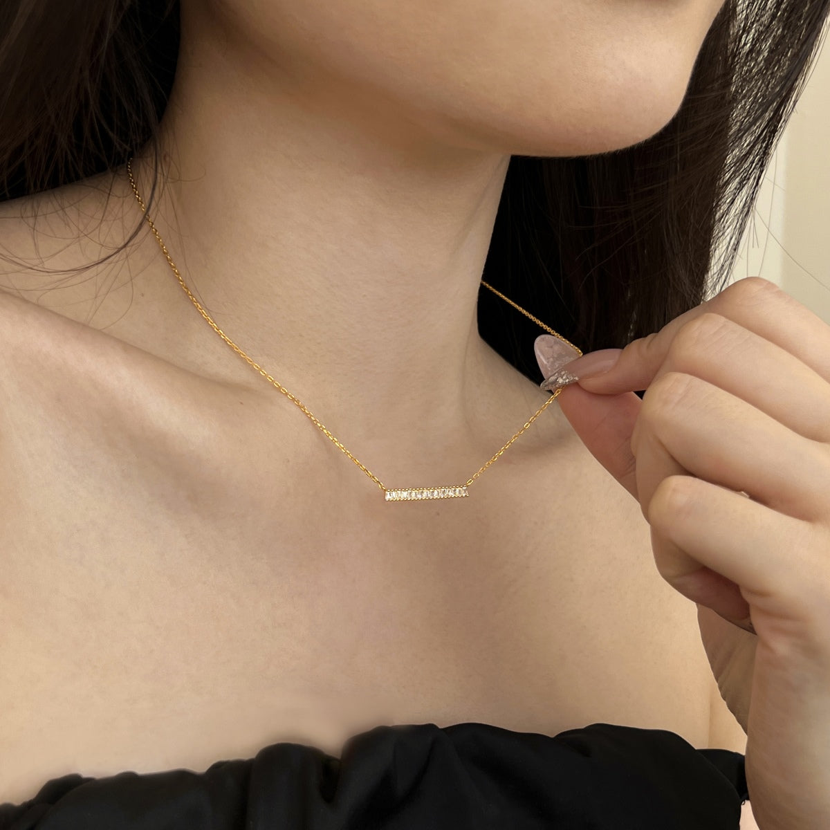 Gold necklace with engraved name on a person wearing a black top.