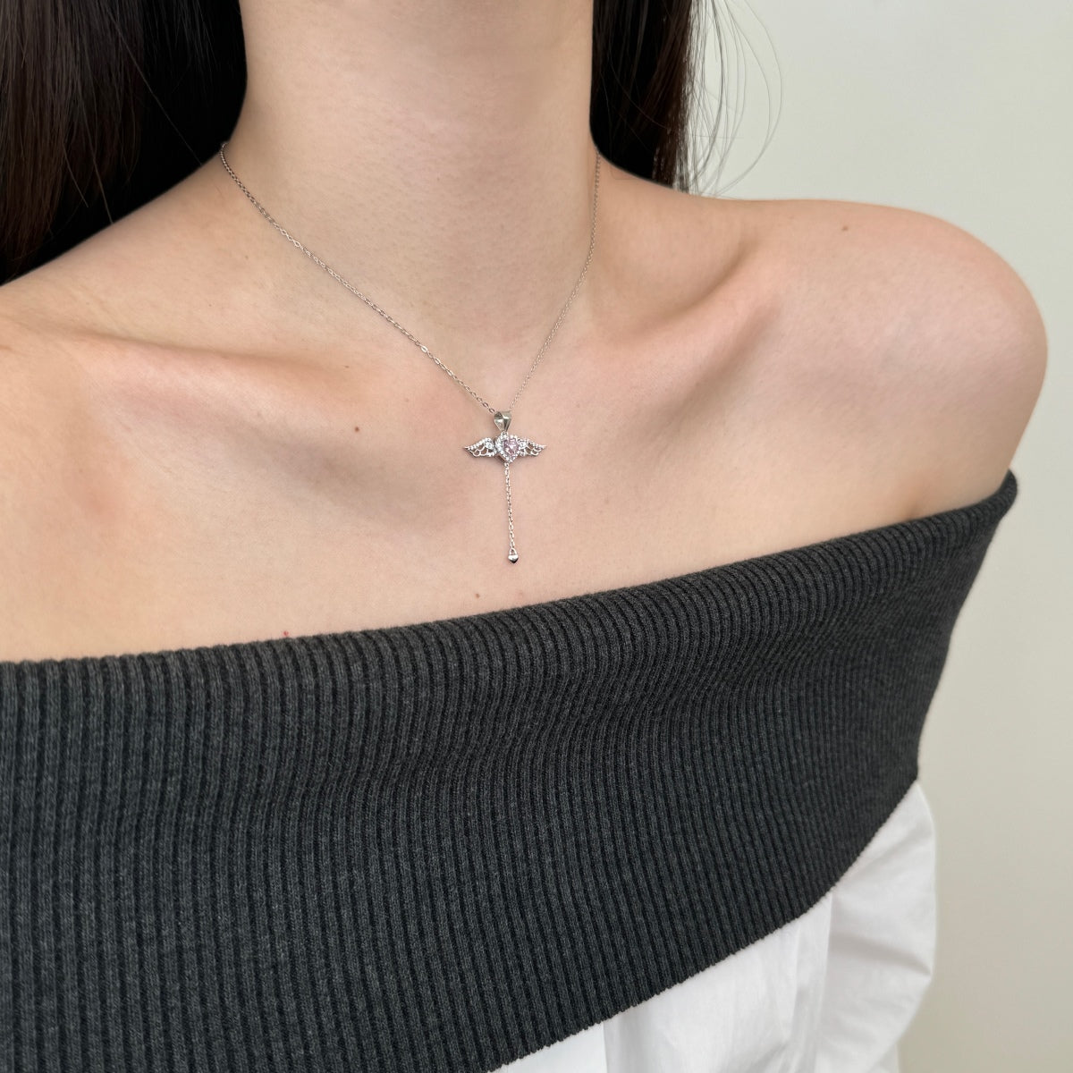 Necklace with a cross pendant worn by a person in a black off-shoulder top.