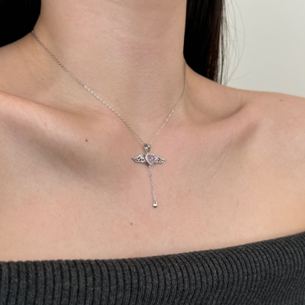 Silver necklace with angle wings pendant worn by a person against a neutral background