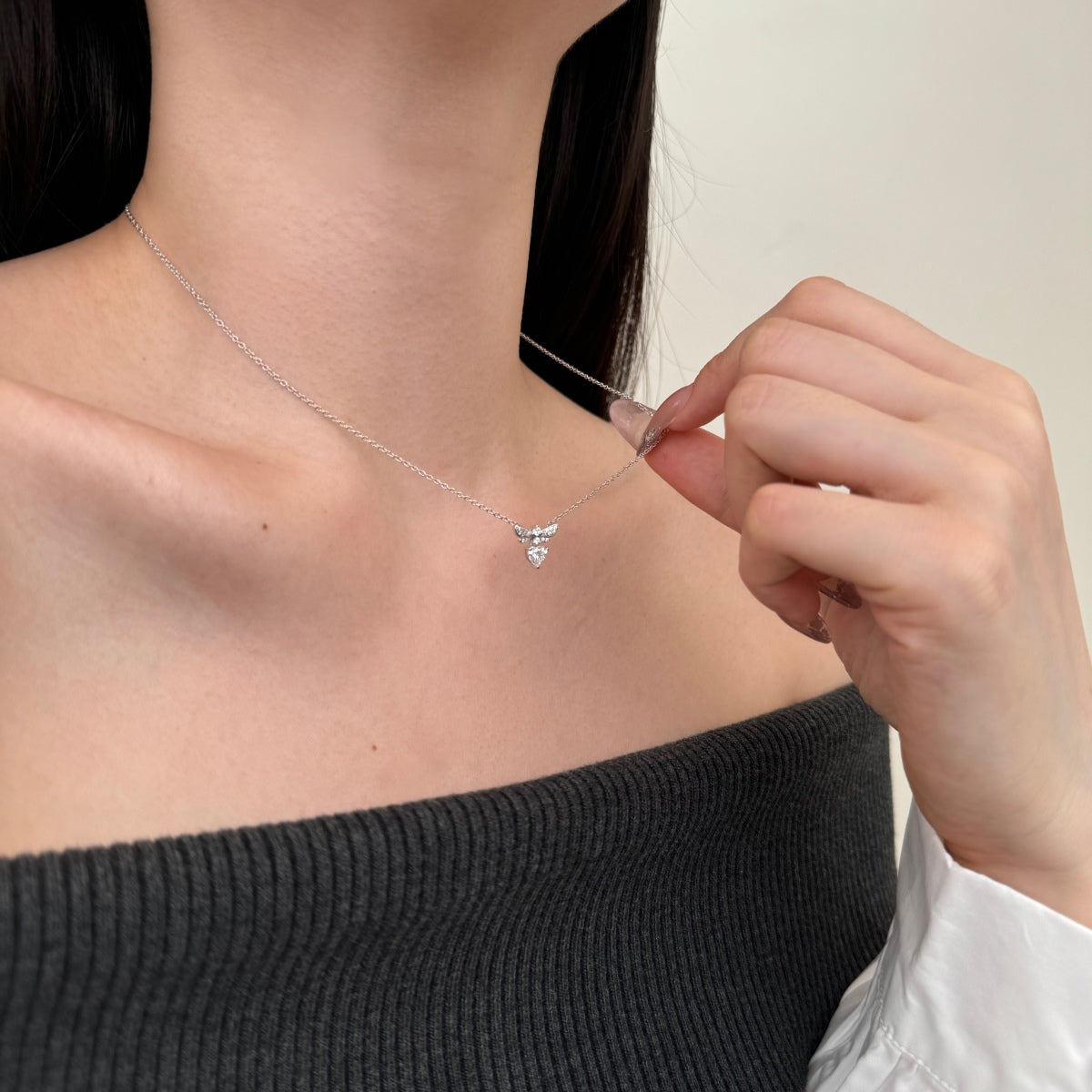Person wearing a silver necklace with a heart-shaped pendant, adjusting it with their hand.