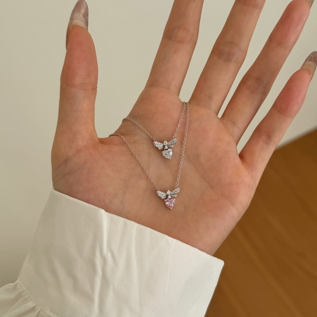 Hand wearing a delicate necklace with butterfly pendants on a neutral background