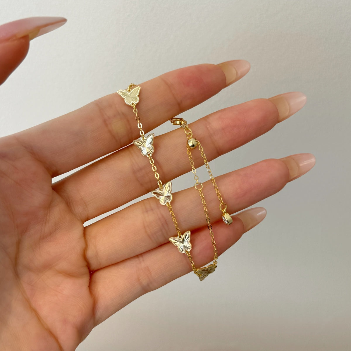 Gold butterfly bracelet on a hand with a neutral background